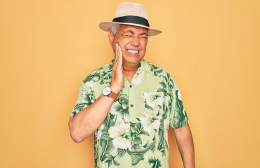 Middle age senior grey-haired man wearing summer hat and floral shirt on beach vacation touching mouth with hand with painful expression because of toothache or dental illness on teeth. Dentist